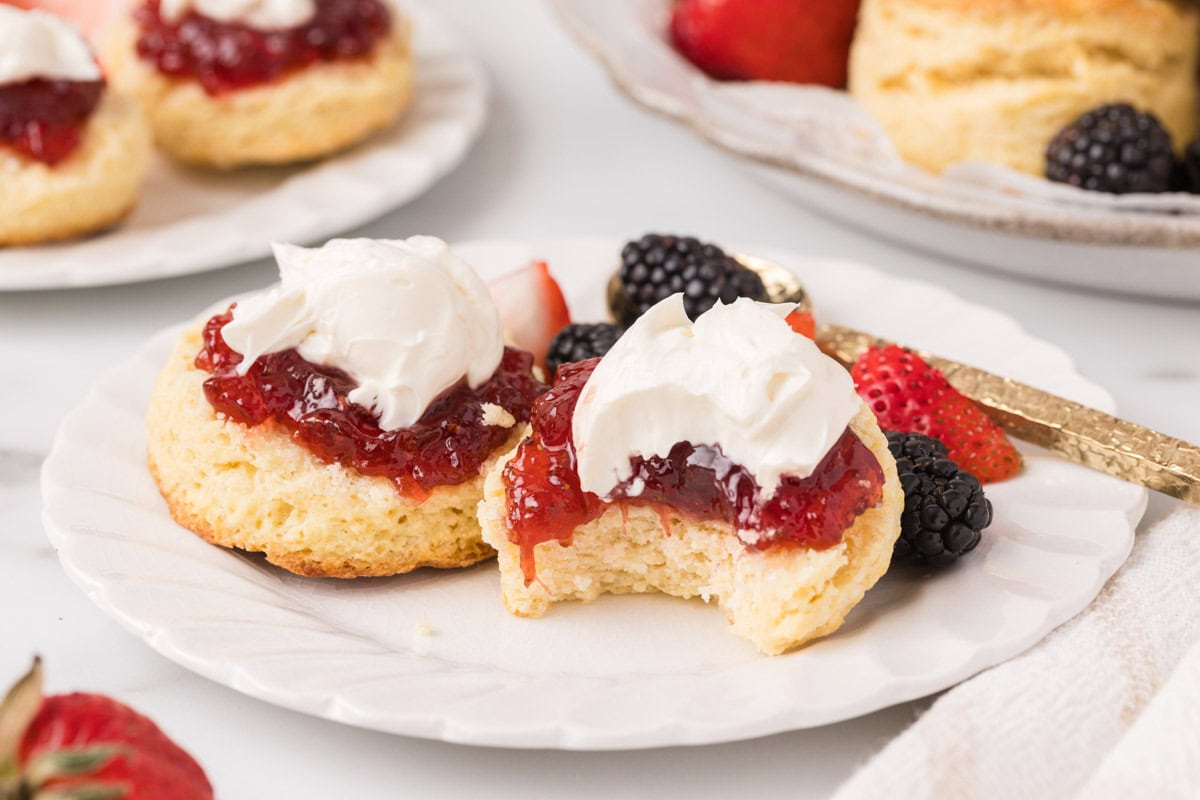 Side view of an English scone with jam and clotted cream, with a bite taken out of it.