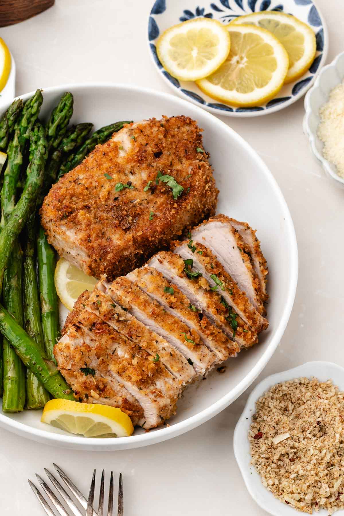 Two parmesan crusted pork chops plated with asparagus, one of the pork chops is sliced.