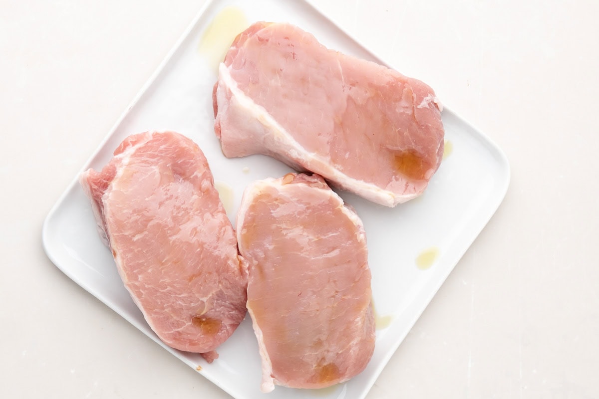 Three pork chops on a place with olive oil on them.