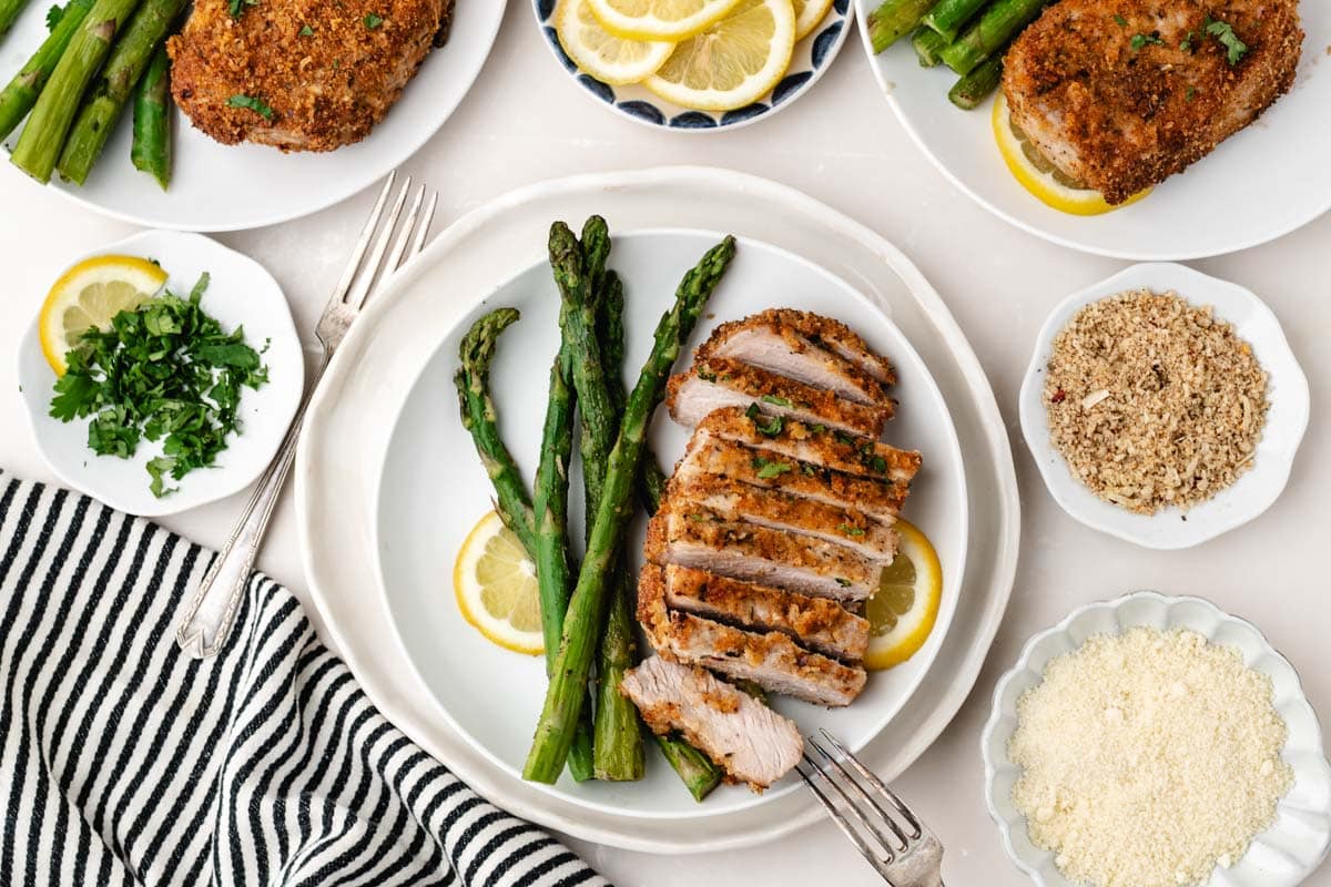 Overhead shot of a sliced parmesan crusted pork chop on a plate with asparagus.