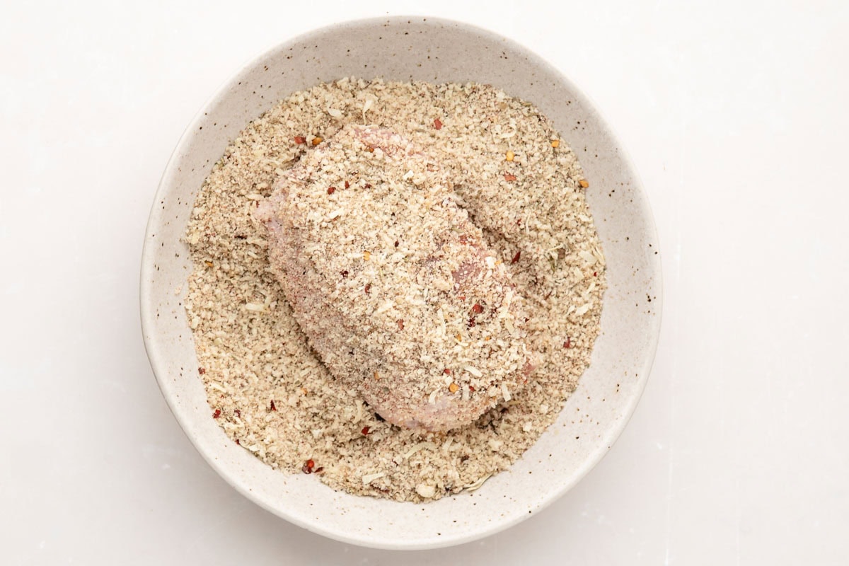 Covering a pork chop in the garlic panko breadcrumb mixture.