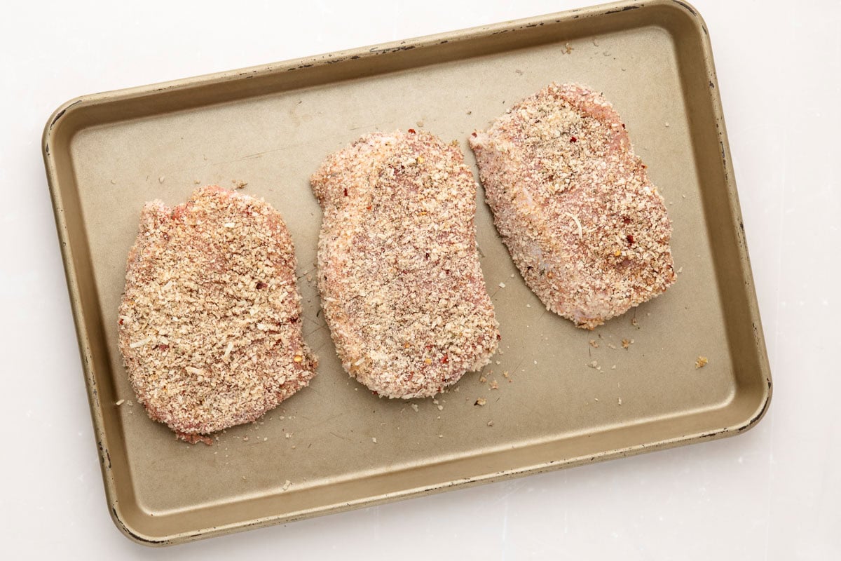 Three panko coated pork chops on a sheet pan.