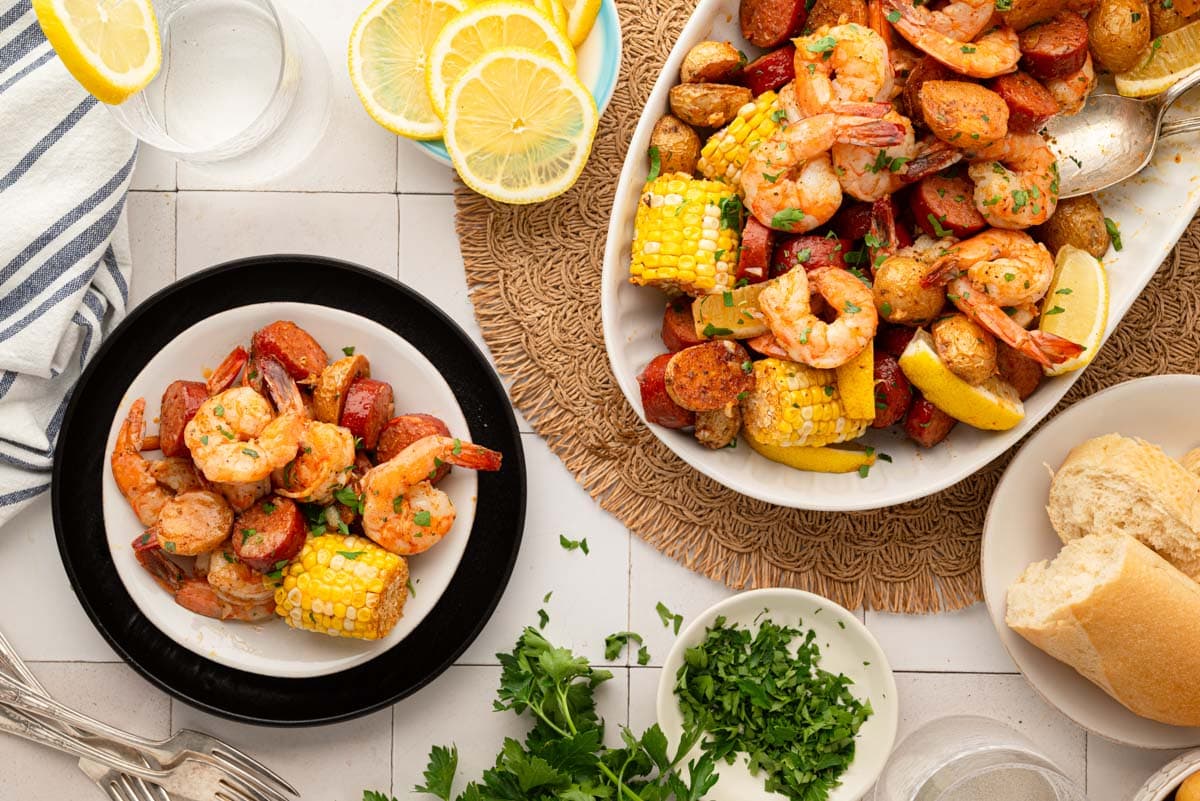 A tablescape with a a serving on a white plate and the platter of the shrimp boil to the side.