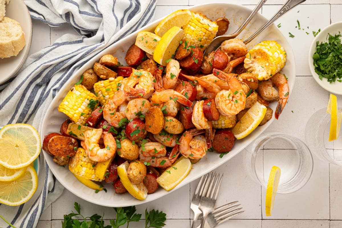 A white serving plate with garlic old bay butter shrimp, corn, potatoes and sausage.