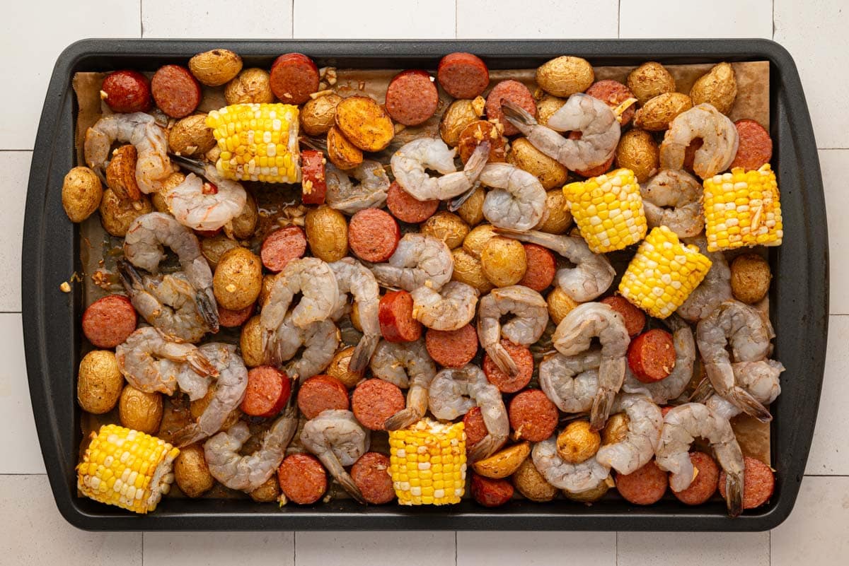 Raw shrimp added to the sheet pan with sauce.
