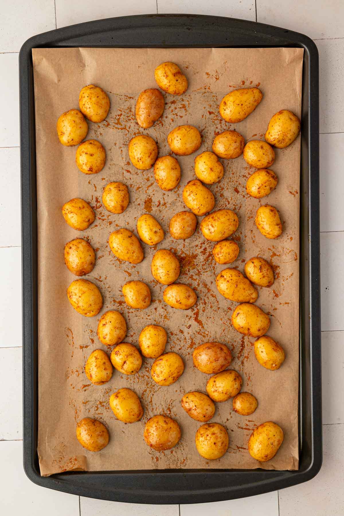 Halved potatoes coated in seasoning on a baking pan lined with parchment paper.