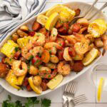 A white serving plate with garlic old bay butter shrimp, corn, potatoes and sausage.