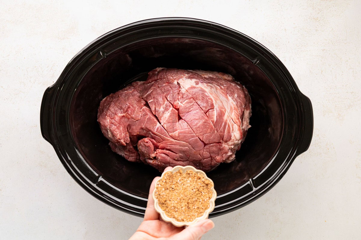 Sprinkling rub on the pork roast in the slow cooker.