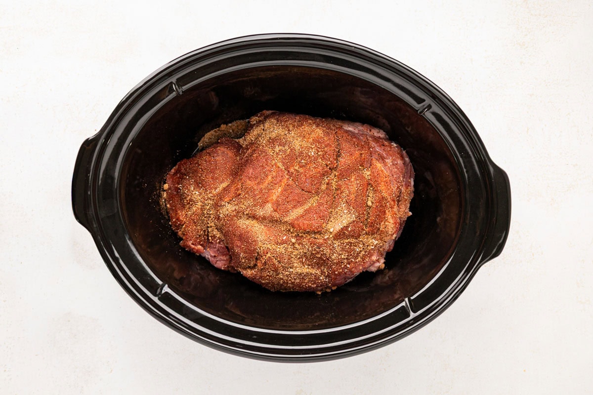 The pork shoulder after being coated on all sides in the slow cooker.