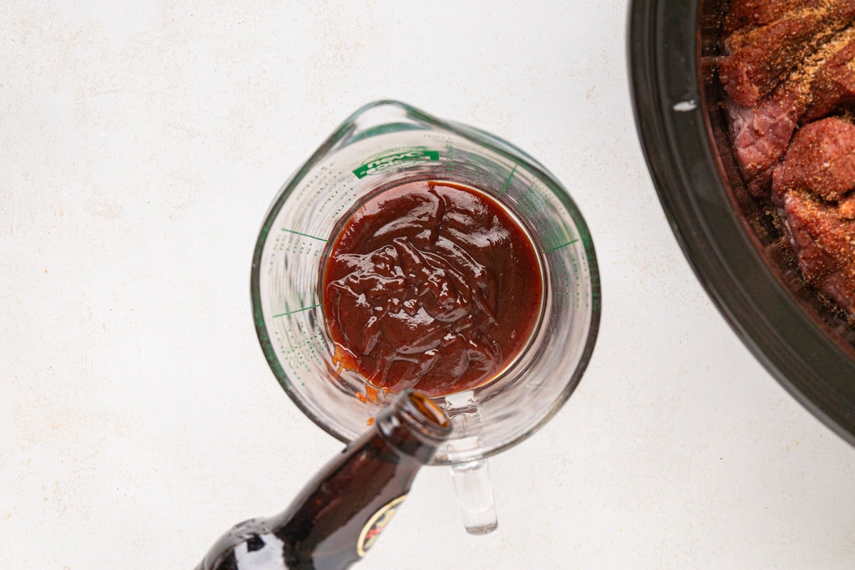 Pouring root beer into a measuring cup with barbecue sauce.