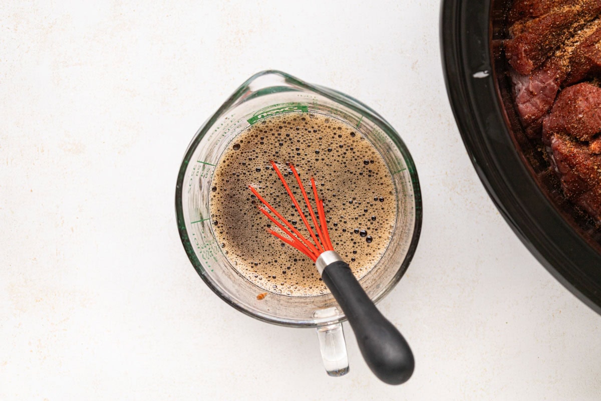 Mixing the bbq sauce and root beer together in a measuring cup with a whisk.