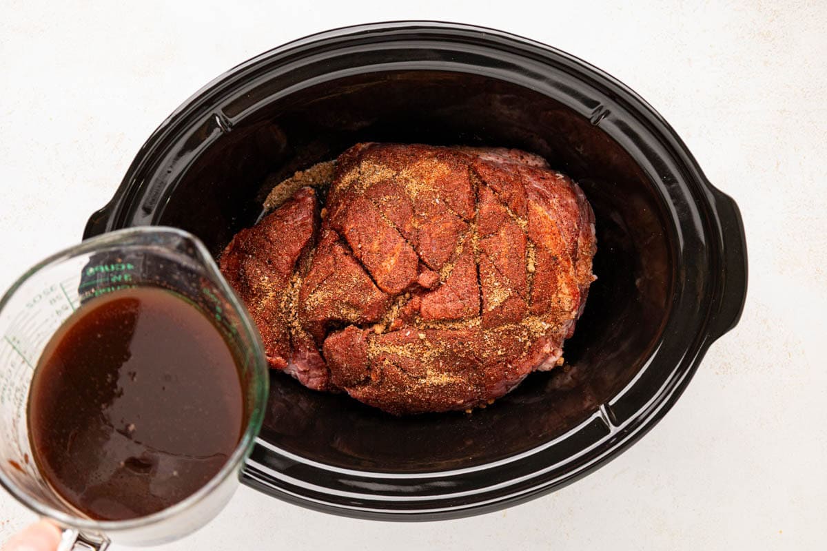 Braising liquid being poured around the pork shoulder.