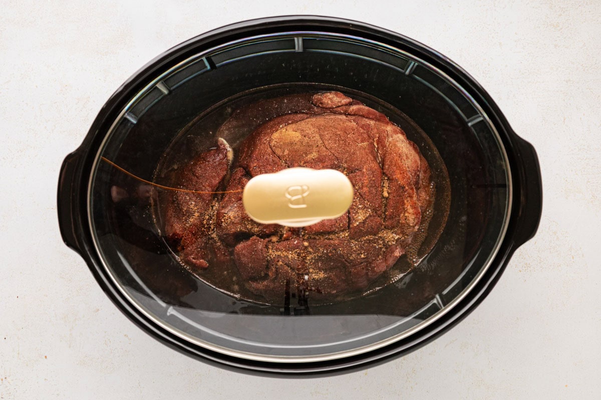 Lid placed on slow cooker with the pork shoulder nestled in the braising liquid.