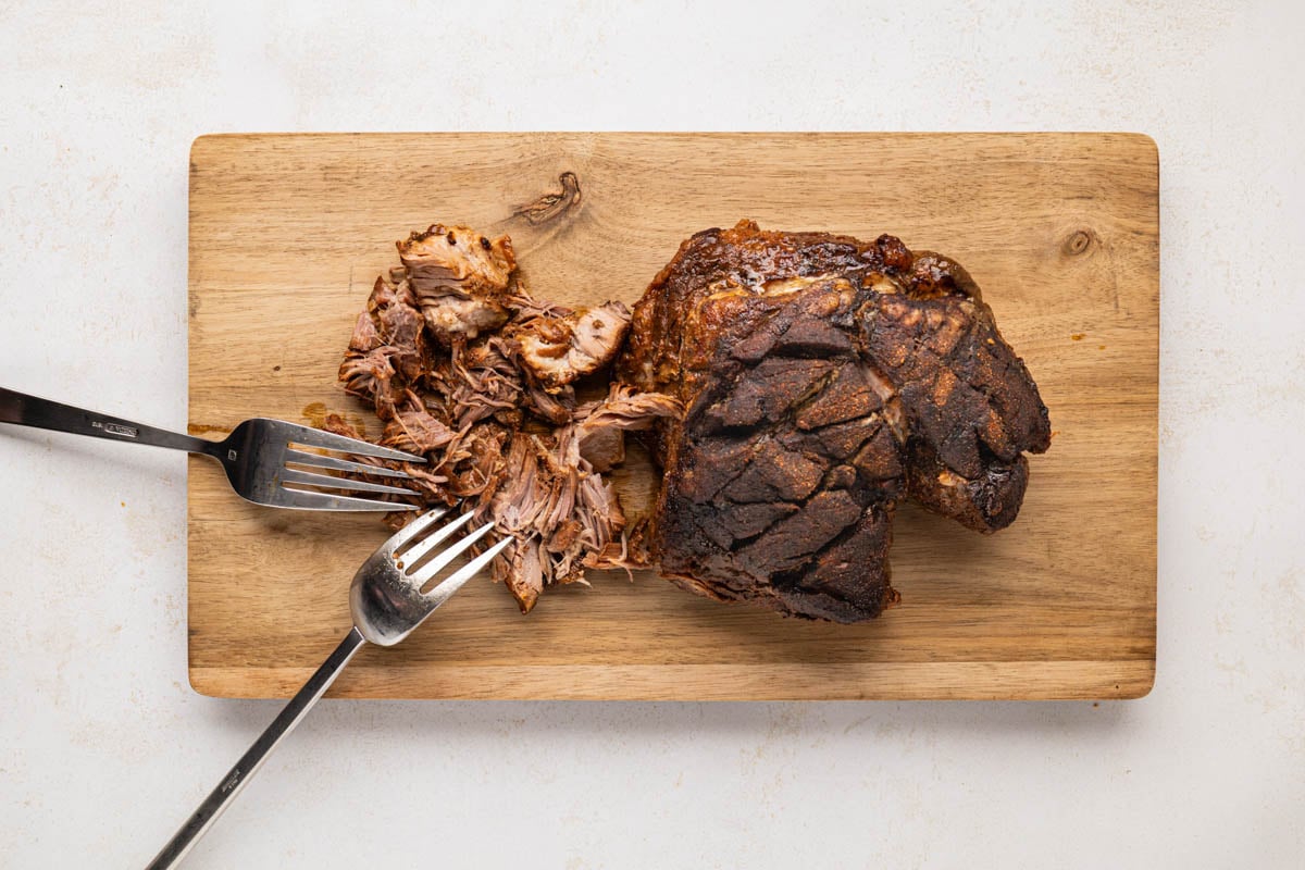 Shredding pork shoulder on a cutting board.