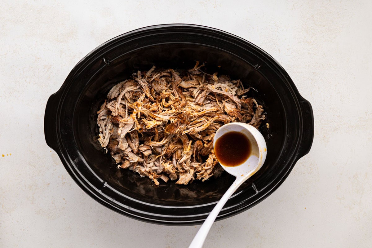 Spooning in some of the cooking liquids over pulled root beer pork.