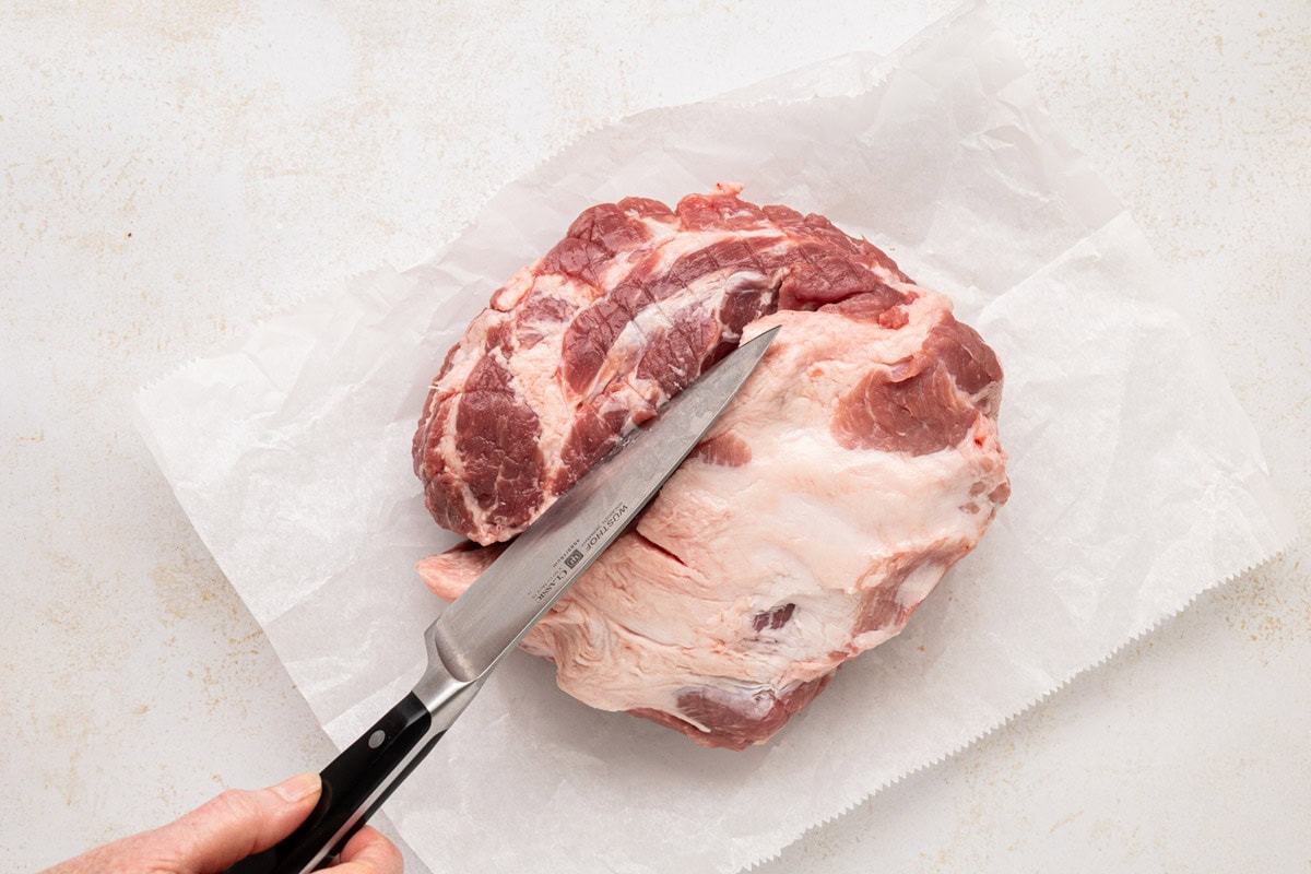 Scoring a pork shoulder with a knife in a criss-cross pattern.