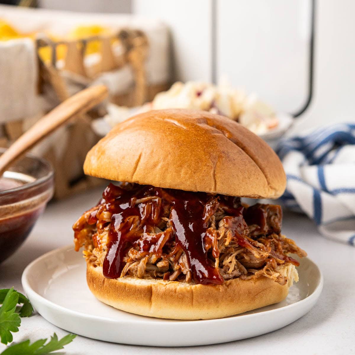 Root beer shredded pork sandwich on a bun with a slow cooker in the background.