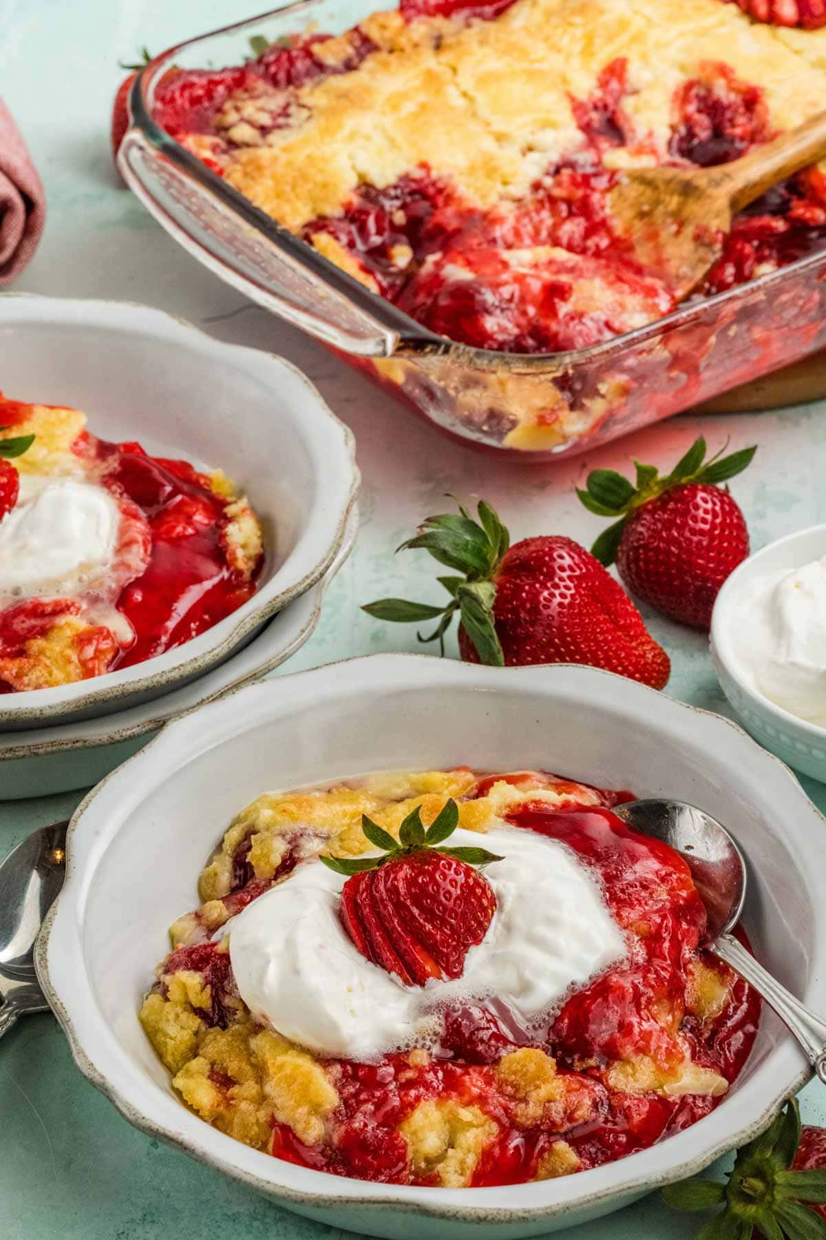 Strawberry dump cake serving in a bowl with the baking dish of cake in the background.