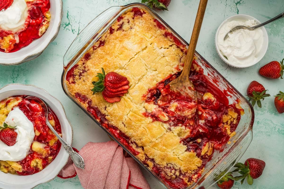 Baked strawberry dump cake in a glass baking dish with a wooden spoon.