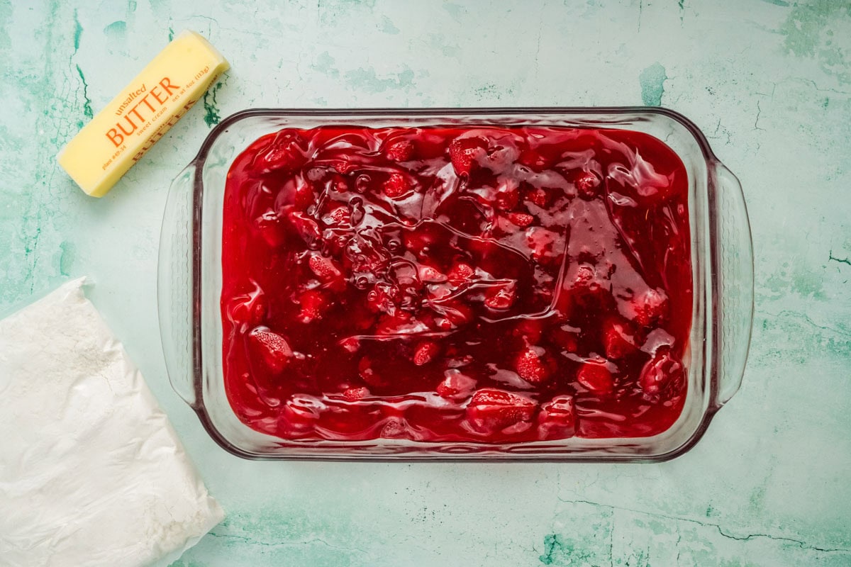 Two cans of strawberry pie filling in a glass baking dish.