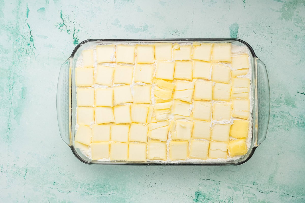Sliced butter lined up on top of the cake mix in a glass baking dish.