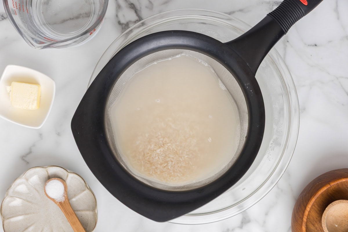 Rice in a fine-mesh strainer with water.