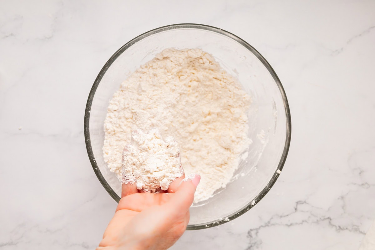 Hand lifting up flour with cold butter cut into it.