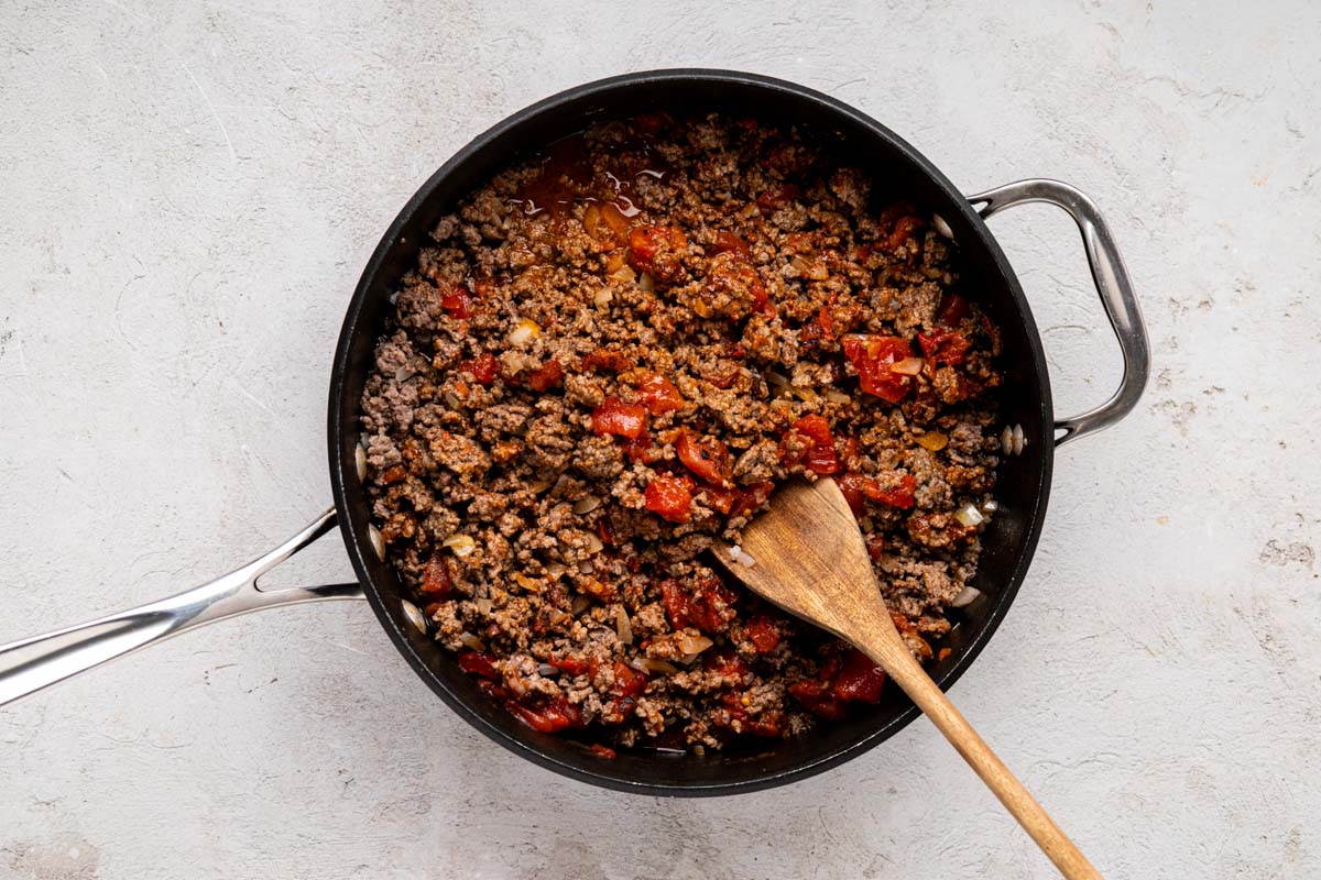 Taco seasoning and fire roasted tomatoes added to ground beef mixture in a skillet.