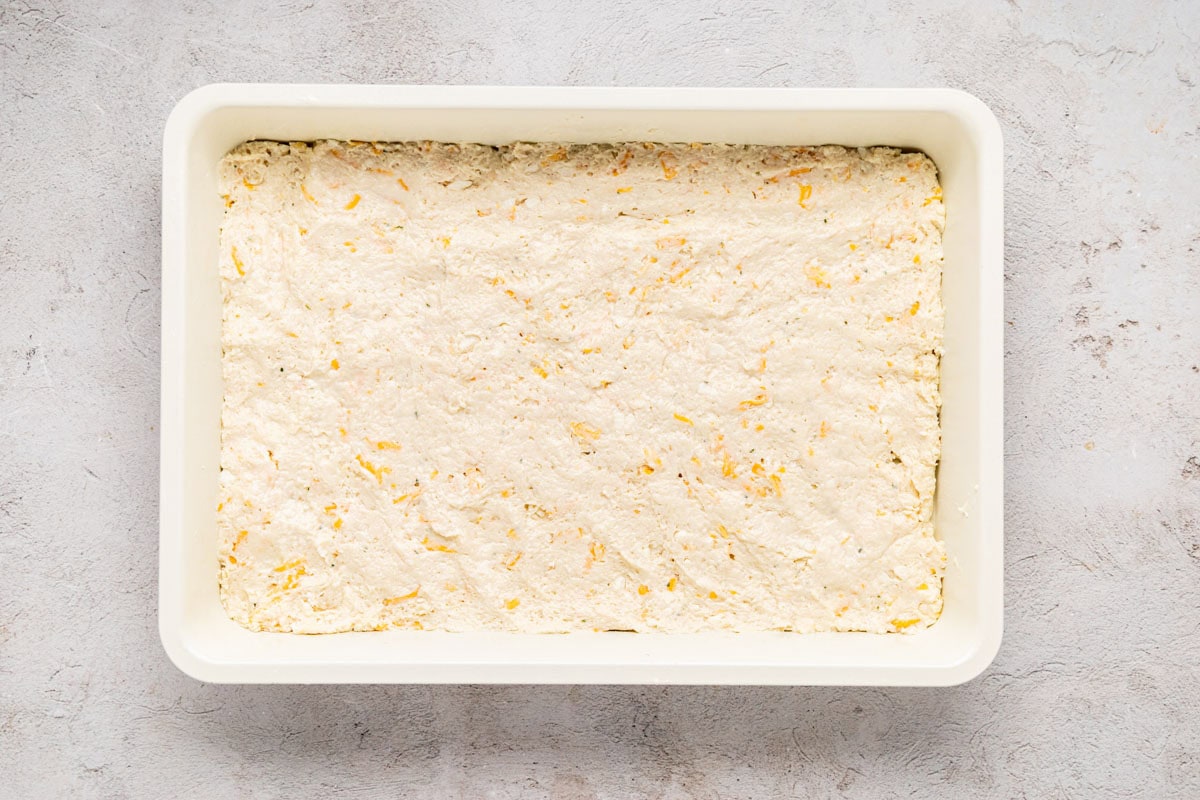 Cheddar bay biscuit dough spread in the bottom of a baking dish.