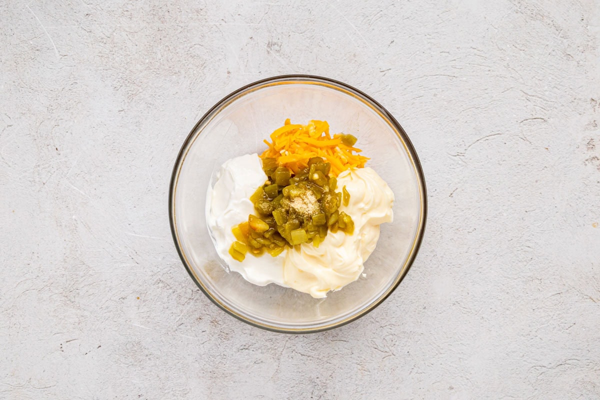 Sour cream, mayo, diced green chiles, and shredded cheese in a small mixing bowl.