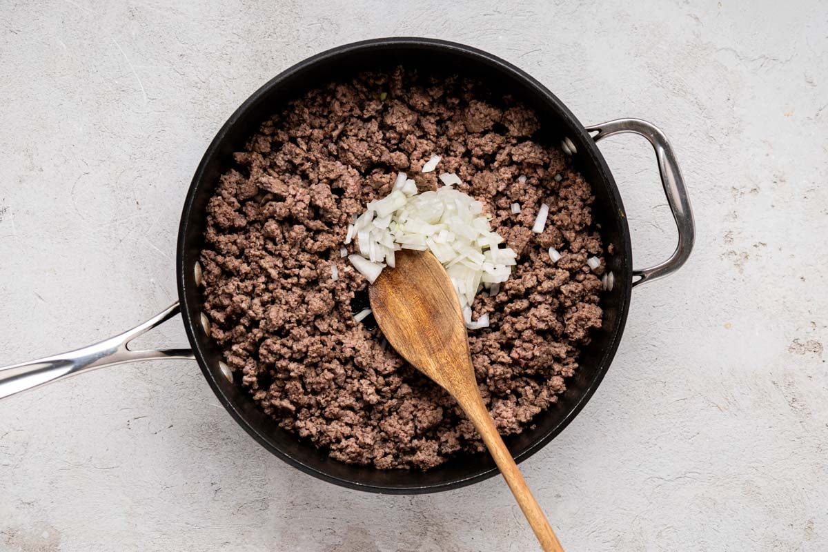 Onions added to browned ground beef in a skillet.