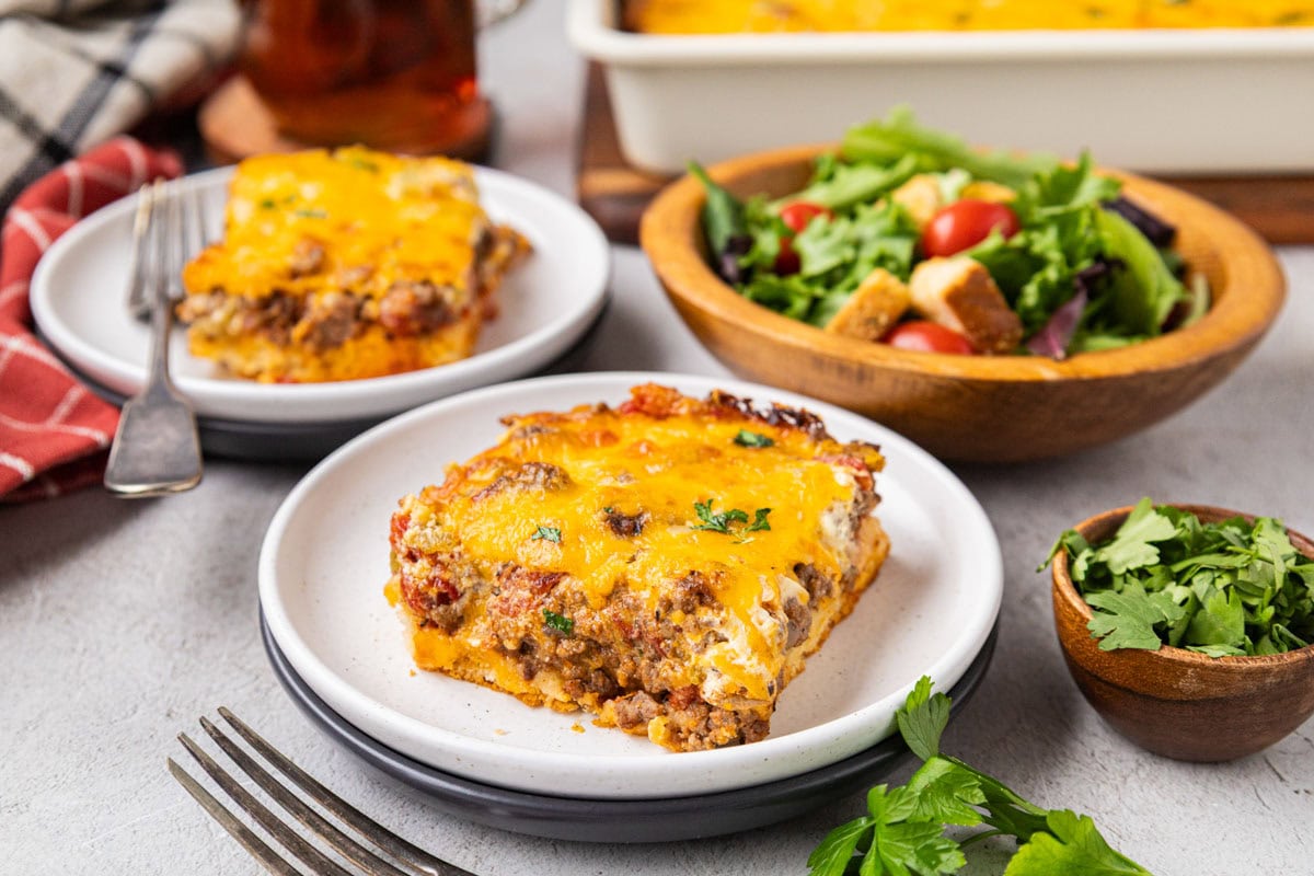Two plates with pieces of cattle drive casserole on them next to a green salad.