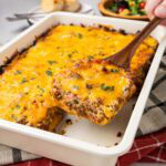 Slice of cattle drive casserole on a wooden spatula being taken from the baking dish.