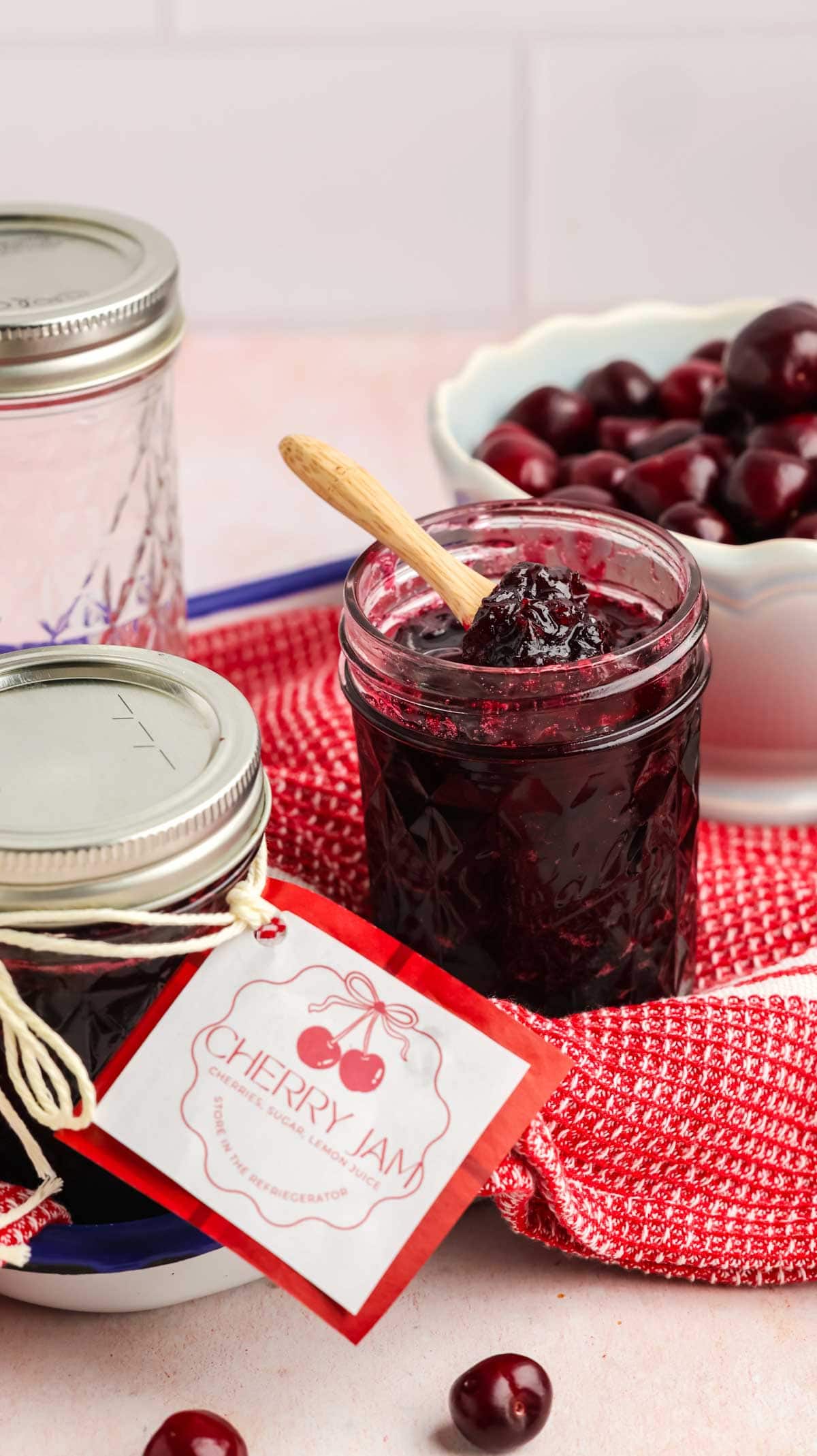 Cherry jam in a jar with a label, with fresh cherries in the background.