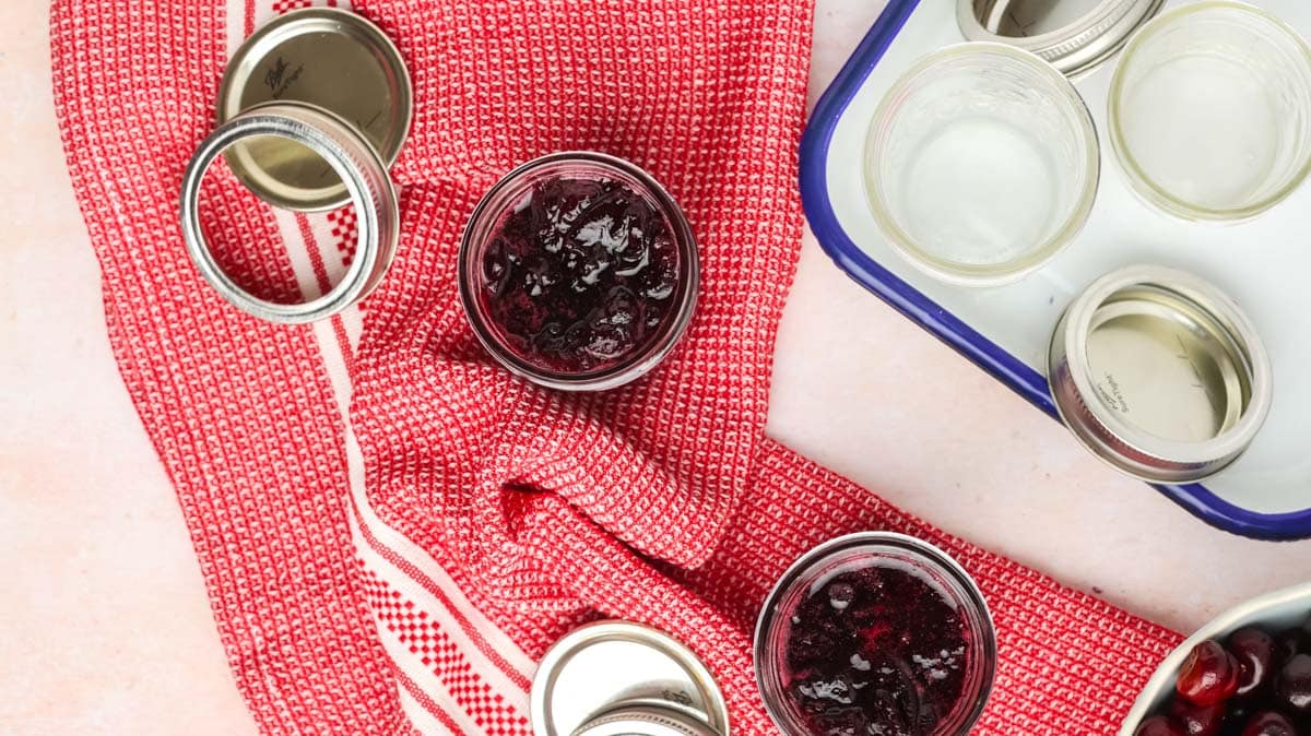 Overhead shot of sterilized jars and some with cherry jam in them.