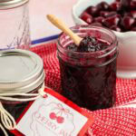 Cherry jam in a glass jar with fresh cherries in the background.