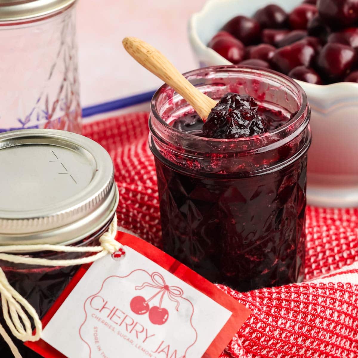 Cherry jam in a glass jar with fresh cherries in the background.