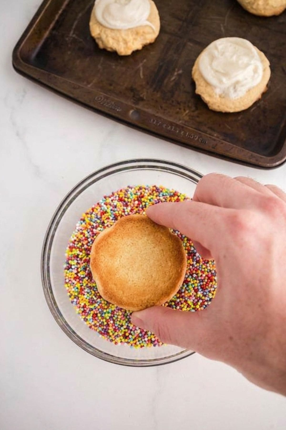 A hand dipping a cooking into nonpareil sprinkles.