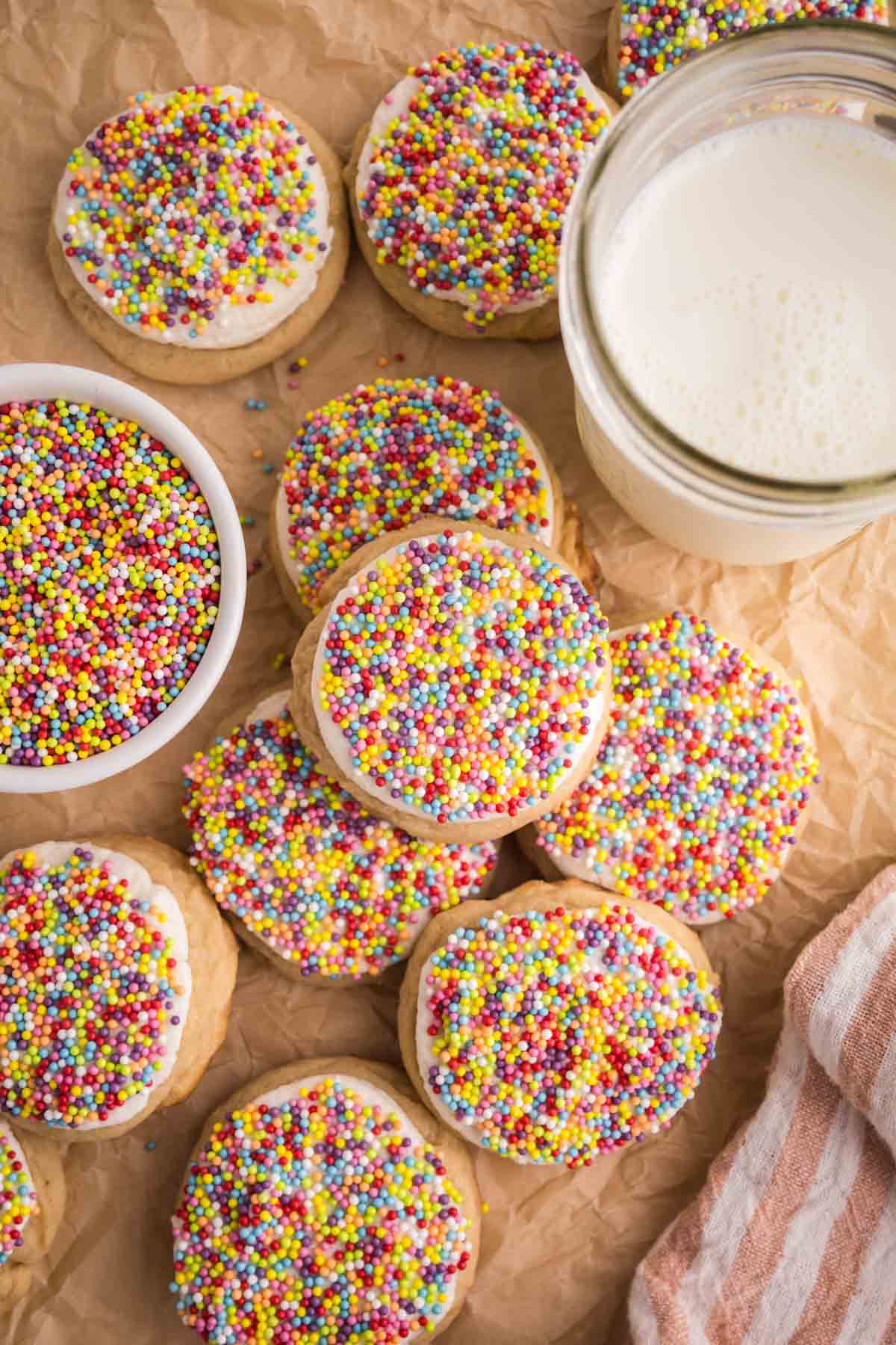 Dot cake cookies scattered on a piece of parchment paper next to a glass of milk.
