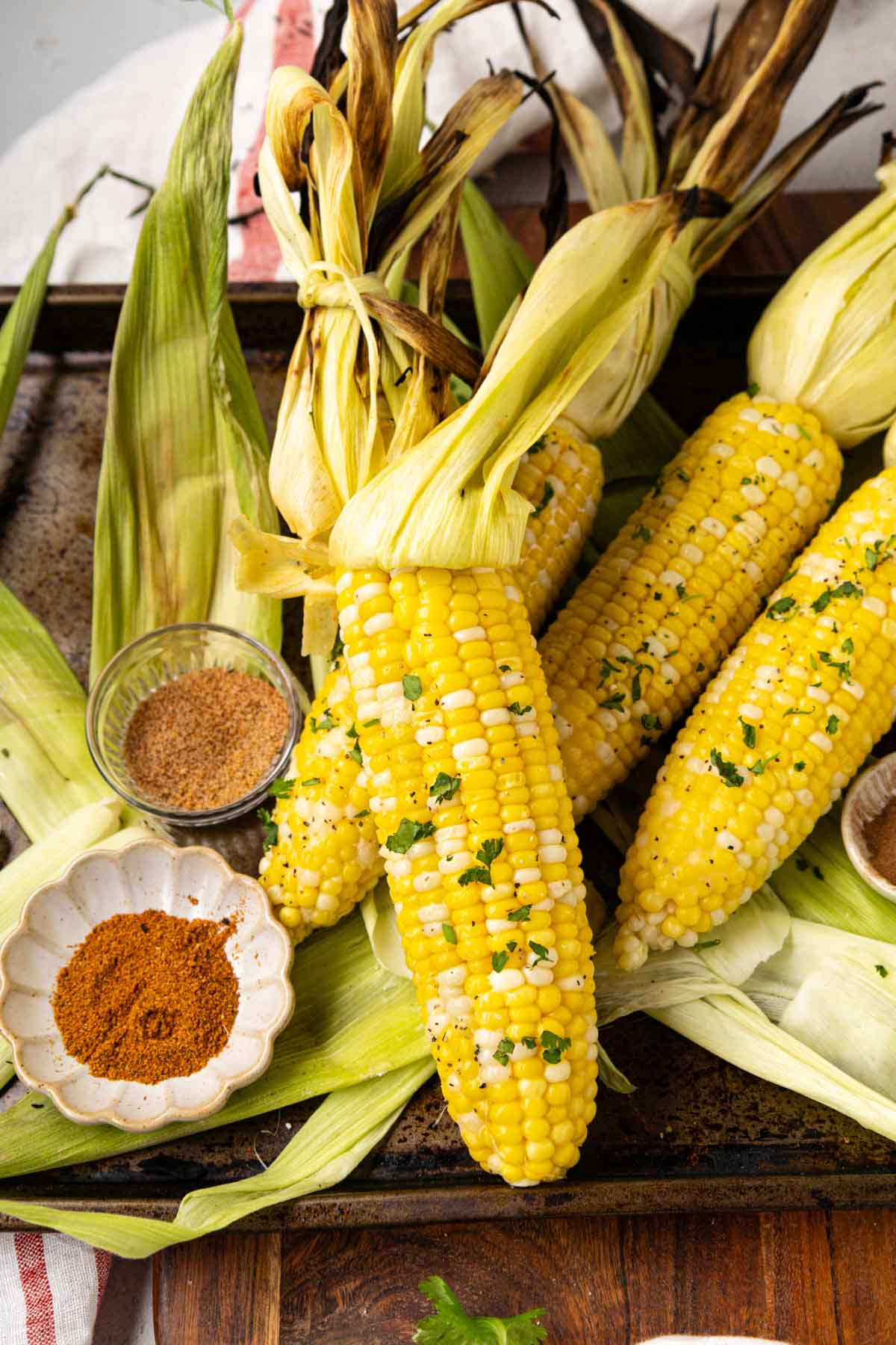 Grilled corn on the cob in the shuck on a platter with seasonings.