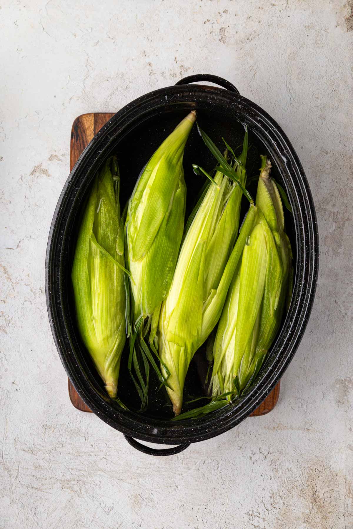Cleaned corn in the shuck in a pot of water.