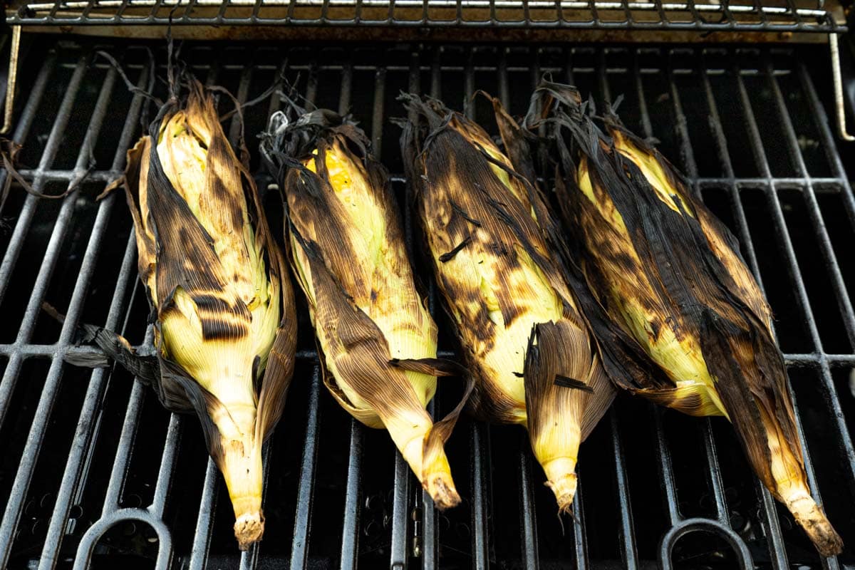 Charred corn in the husk on a grill.