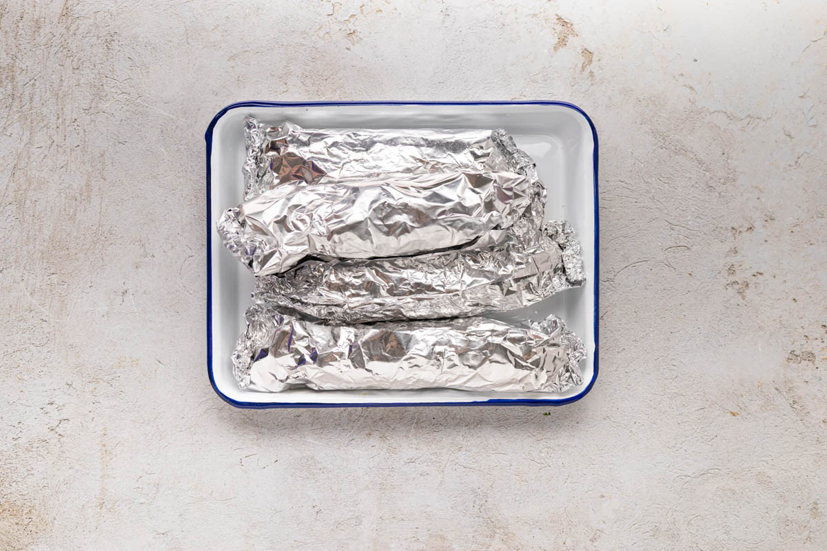 Corn on cob wrapped in foil on a tray.