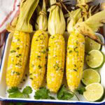Four ears of grilled corn on the cob on a white platter.