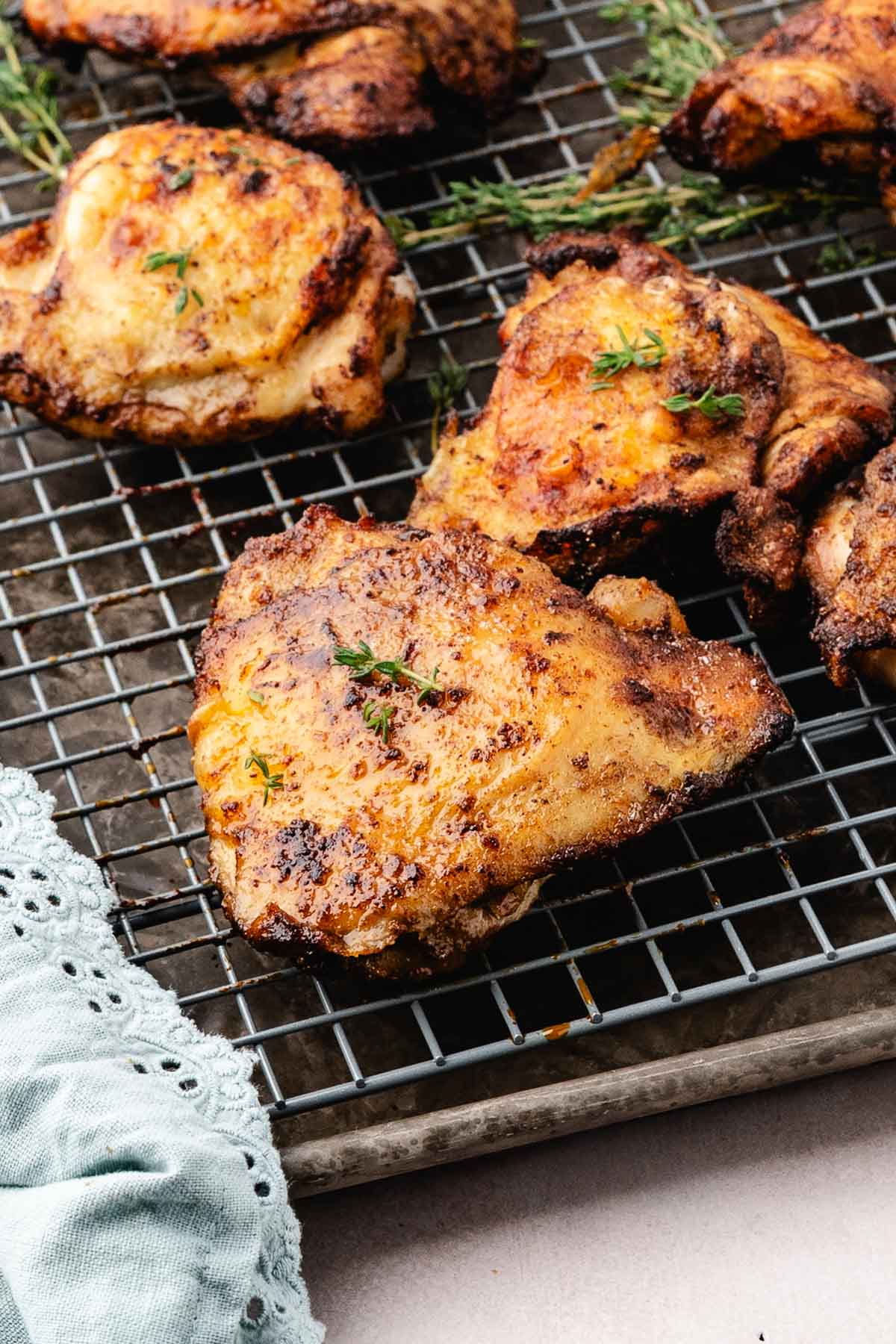 Crispy baked chicken thighs on a wire rack, garnished with thyme.