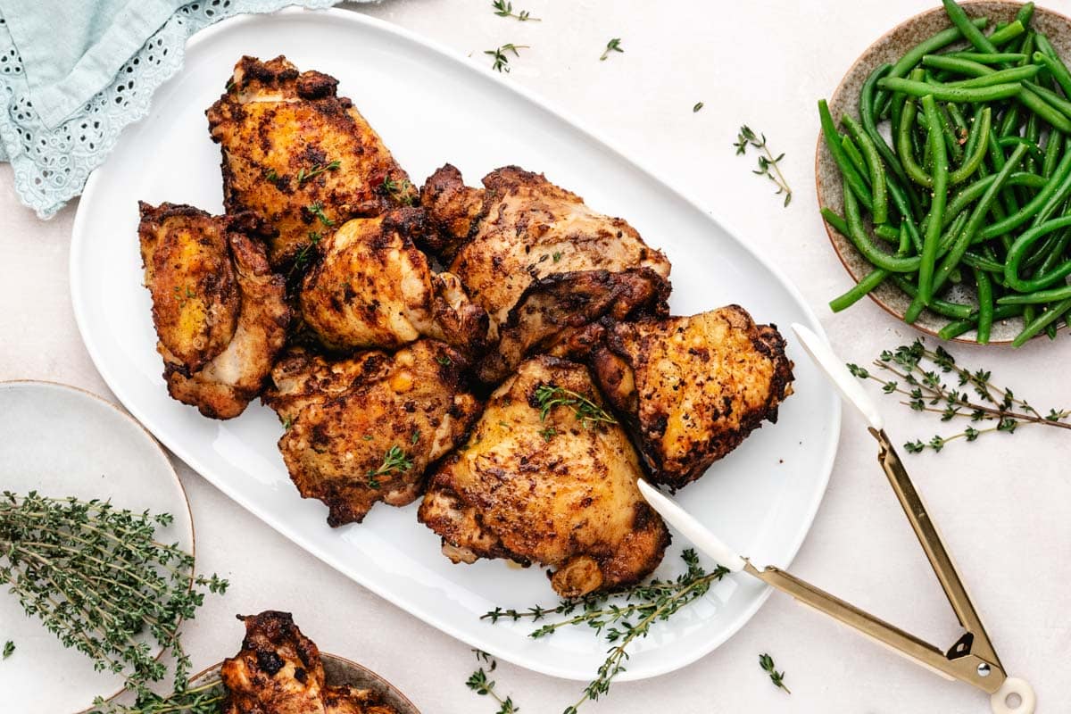 Overhead shot of baked chicken thighs on a serving platter next to a bowl of green beans.