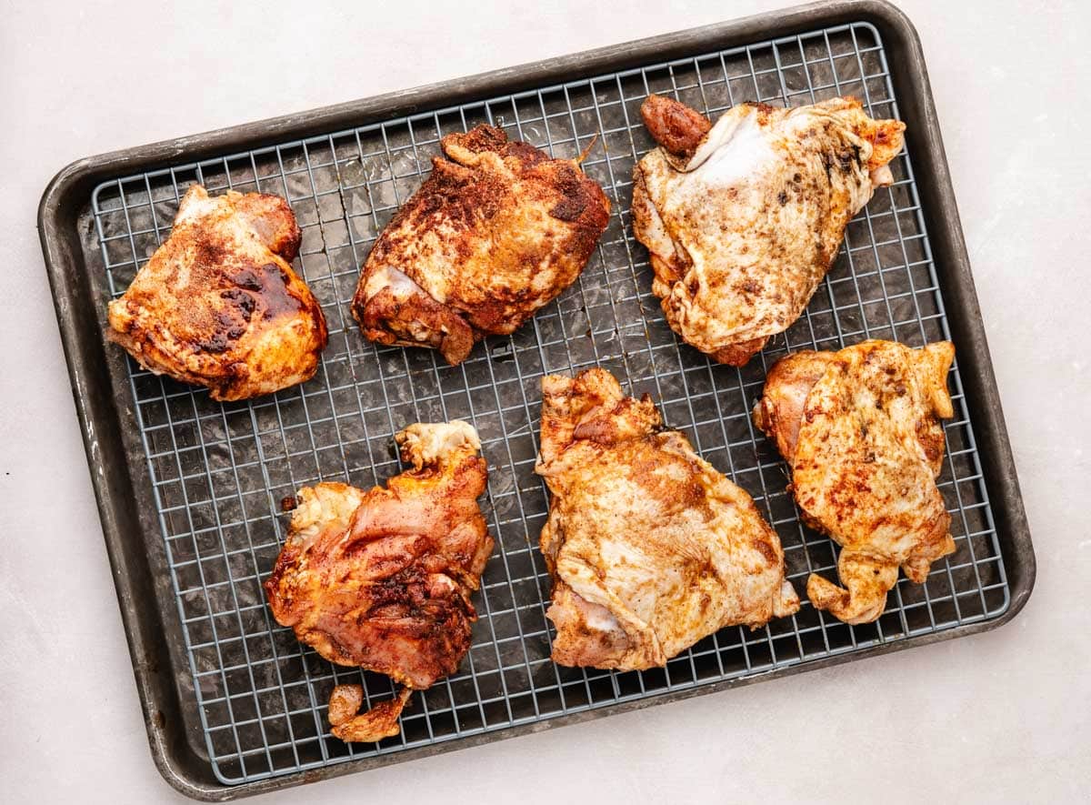 Seasoned chicken thighs placed on a sheet pan lined with a wire rack.