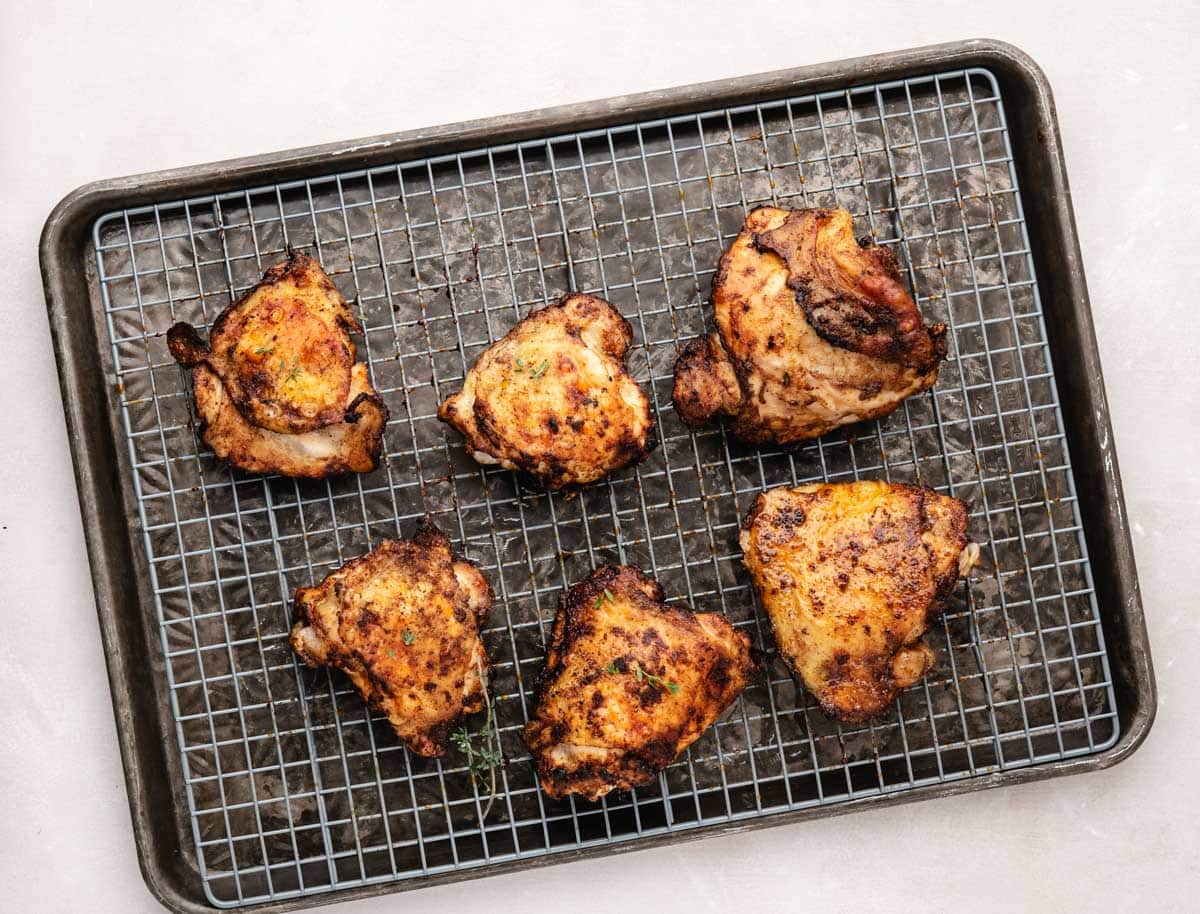 Baked crispy chicken thighs on a sheet pan lined with a wire rack.