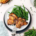 Two baked chicken thighs served with green beans on a plate.