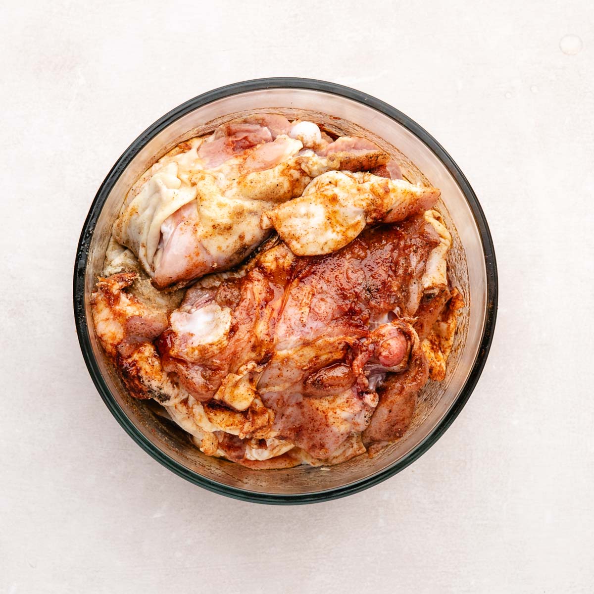 Chicken thighs mixed with spices in a bowl.